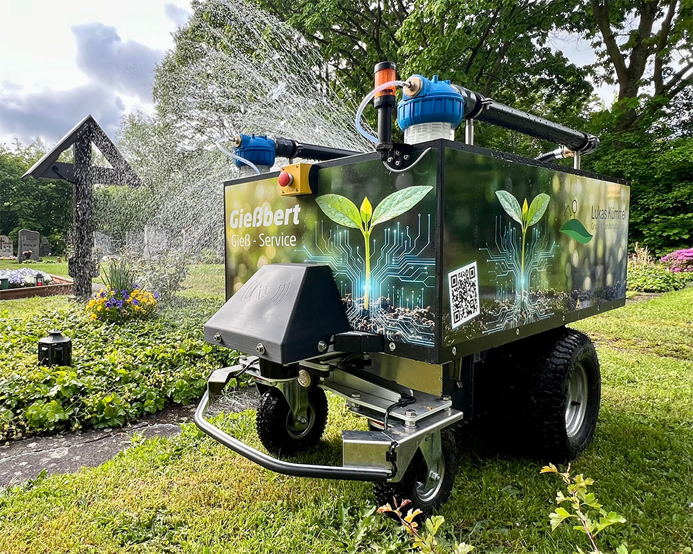 Inmitten verschiedenster anderer Blumen pflanz ein Gärtner frische gelb blühende Blumen in dunkle Erde.